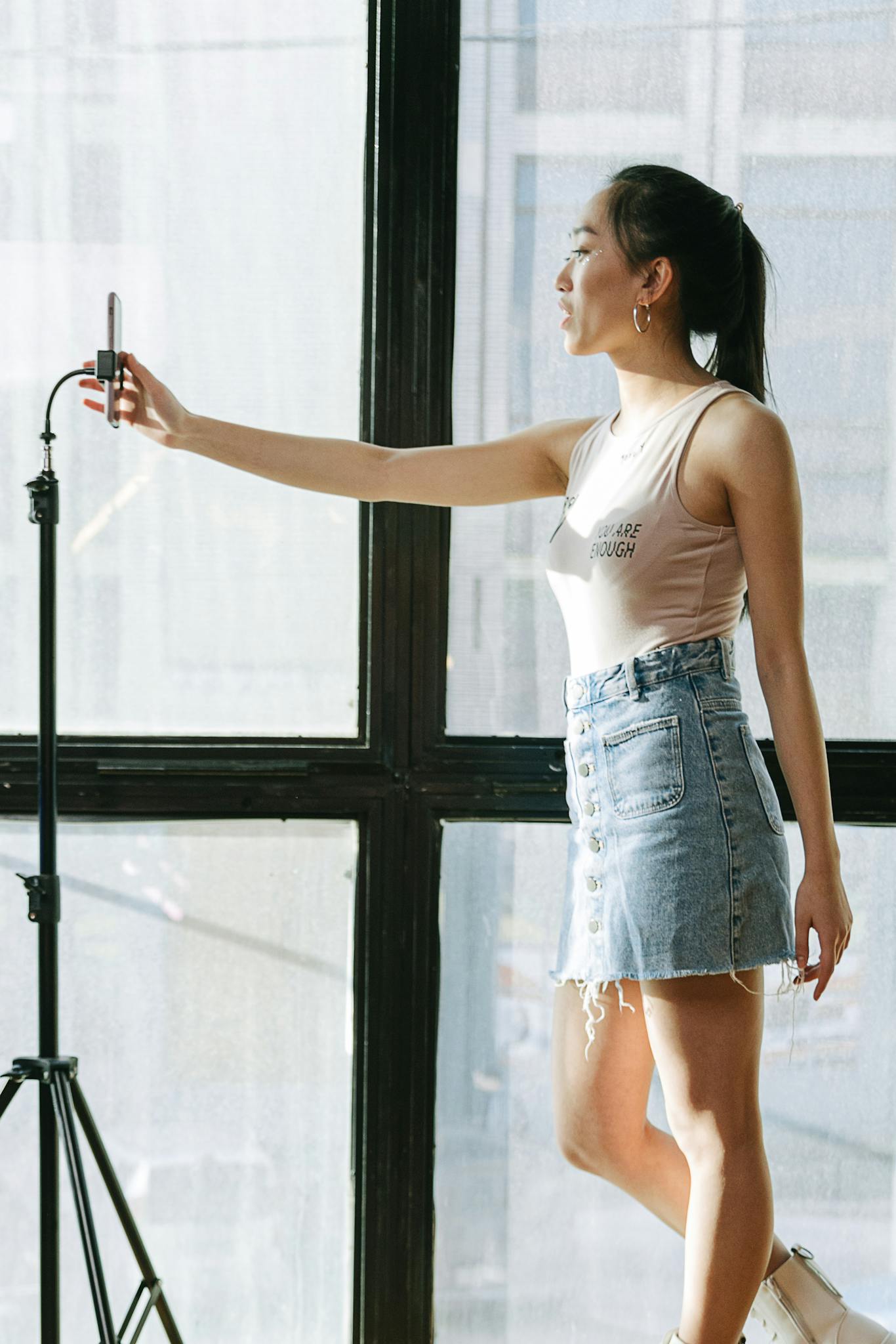 Asian woman filming herself indoors using a mobile phone on a tripod.