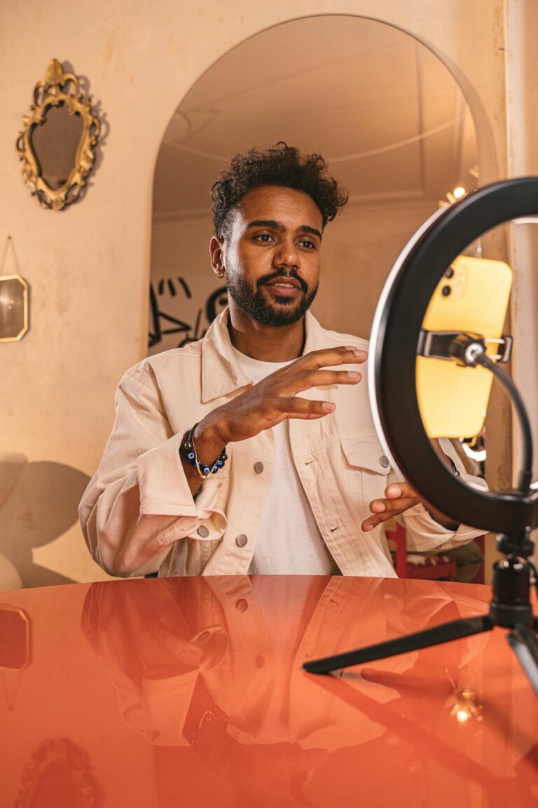Man in beige jacket using ring light setup for video call indoors.