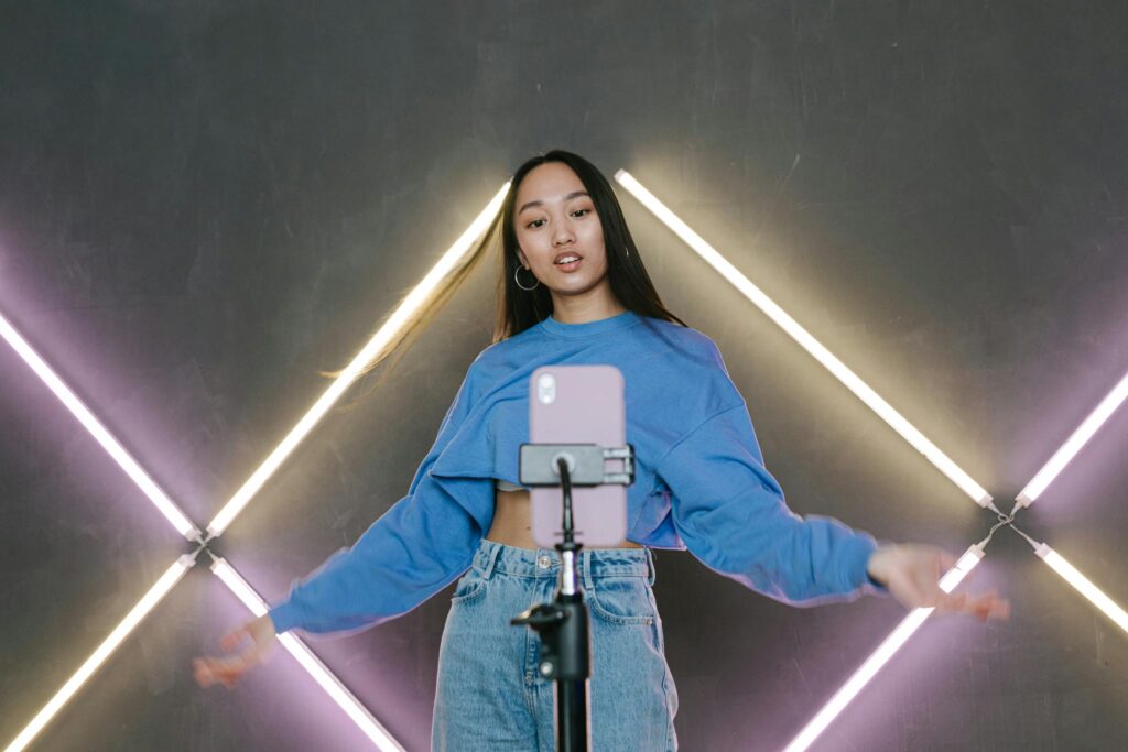 Teen influencer dances stylishly indoors, creating content using smartphone and ring light.